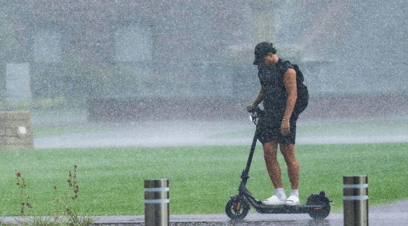 An image of a student riding a scooter in heavy rain without a rain coat or umbrella