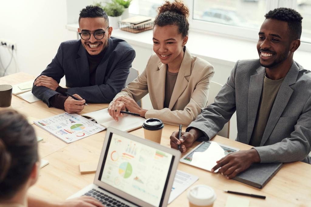 Professional meeting with three smiling people at a table with a laptop open.