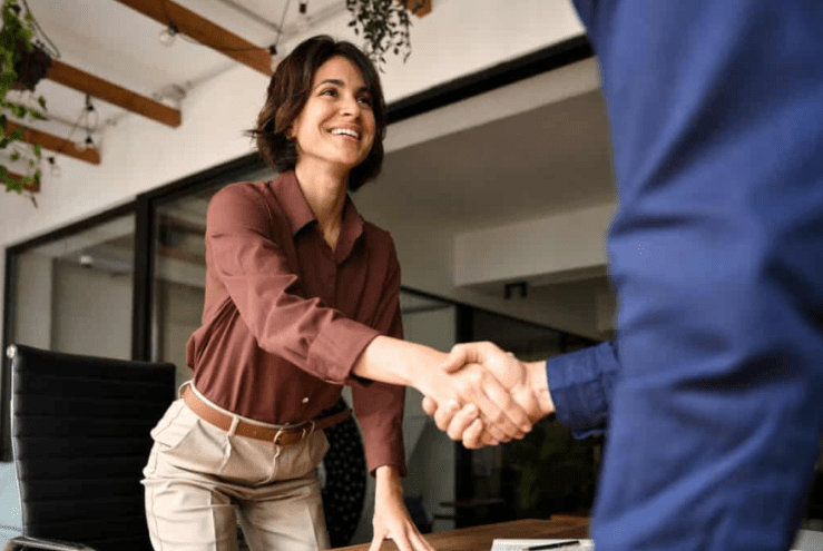 A business professional dressed woman shaking hands with a man in a blue suit.