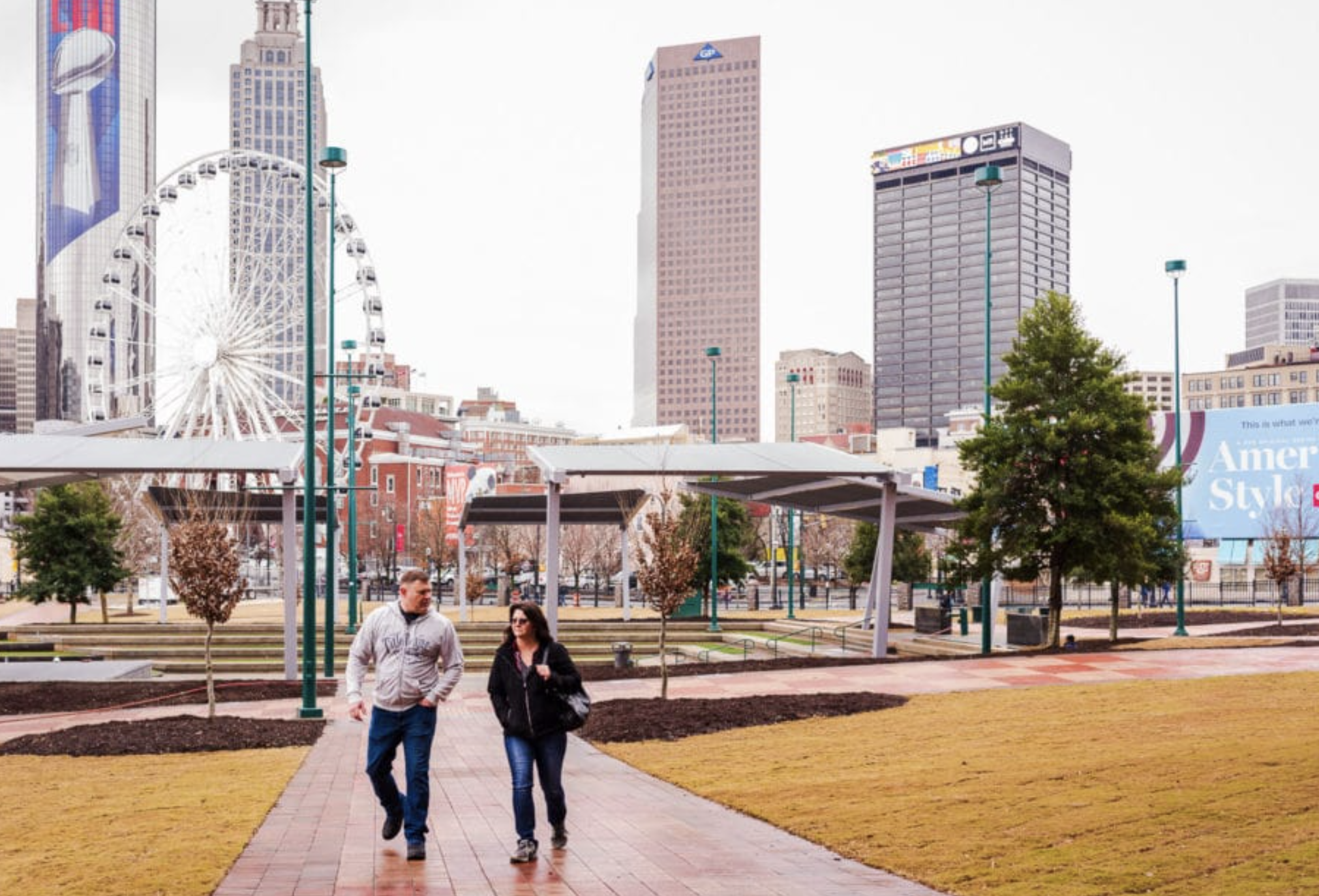 A couple walking through Centennial Olympic Park in Atlanta, with a ferris wheel and the greater Metro Atlanta skyline behind them