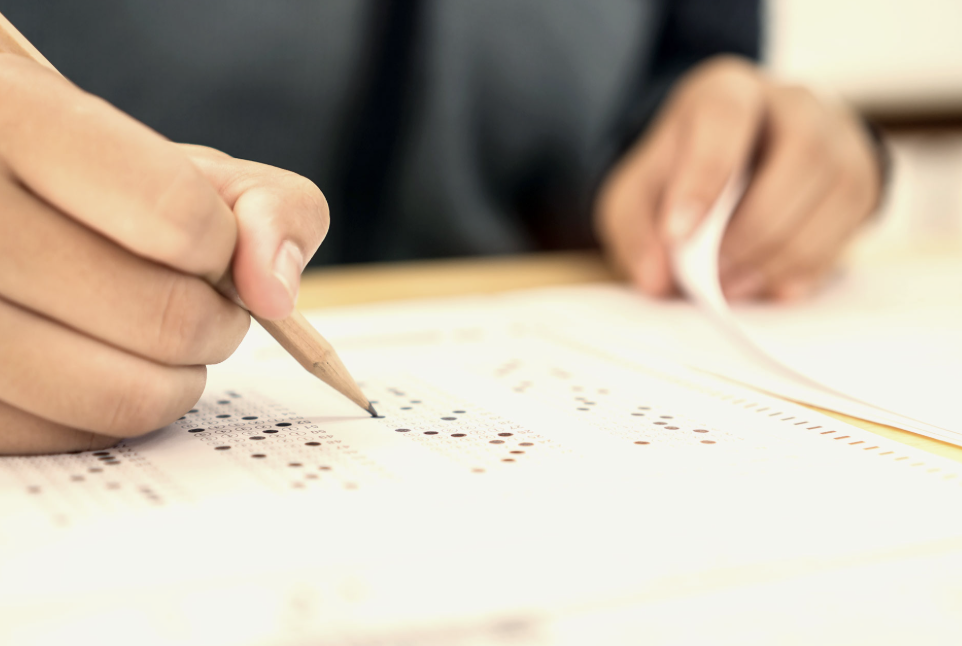 A top-down shot of a student using a pencil to take a multi-page multiple choice examination
