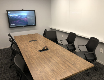 An image that shows a room with a television placed on the wall and 6 seats arranged in front of it, separated by a table.