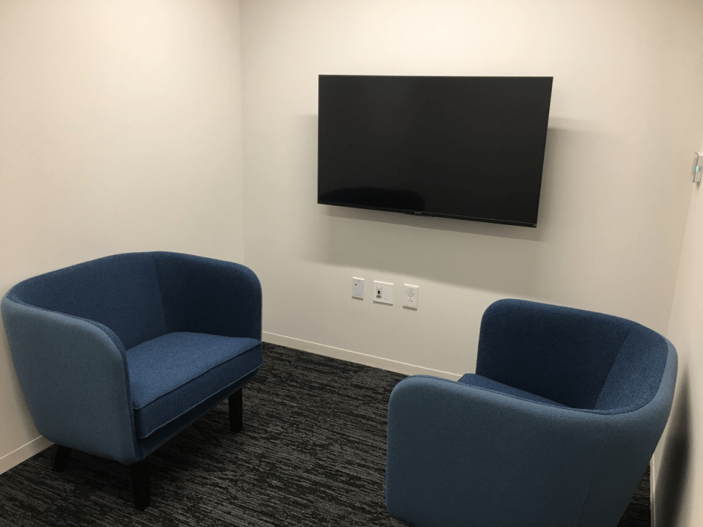 An image that shows a room with a television placed on the wall and two seats arranged in front of it.