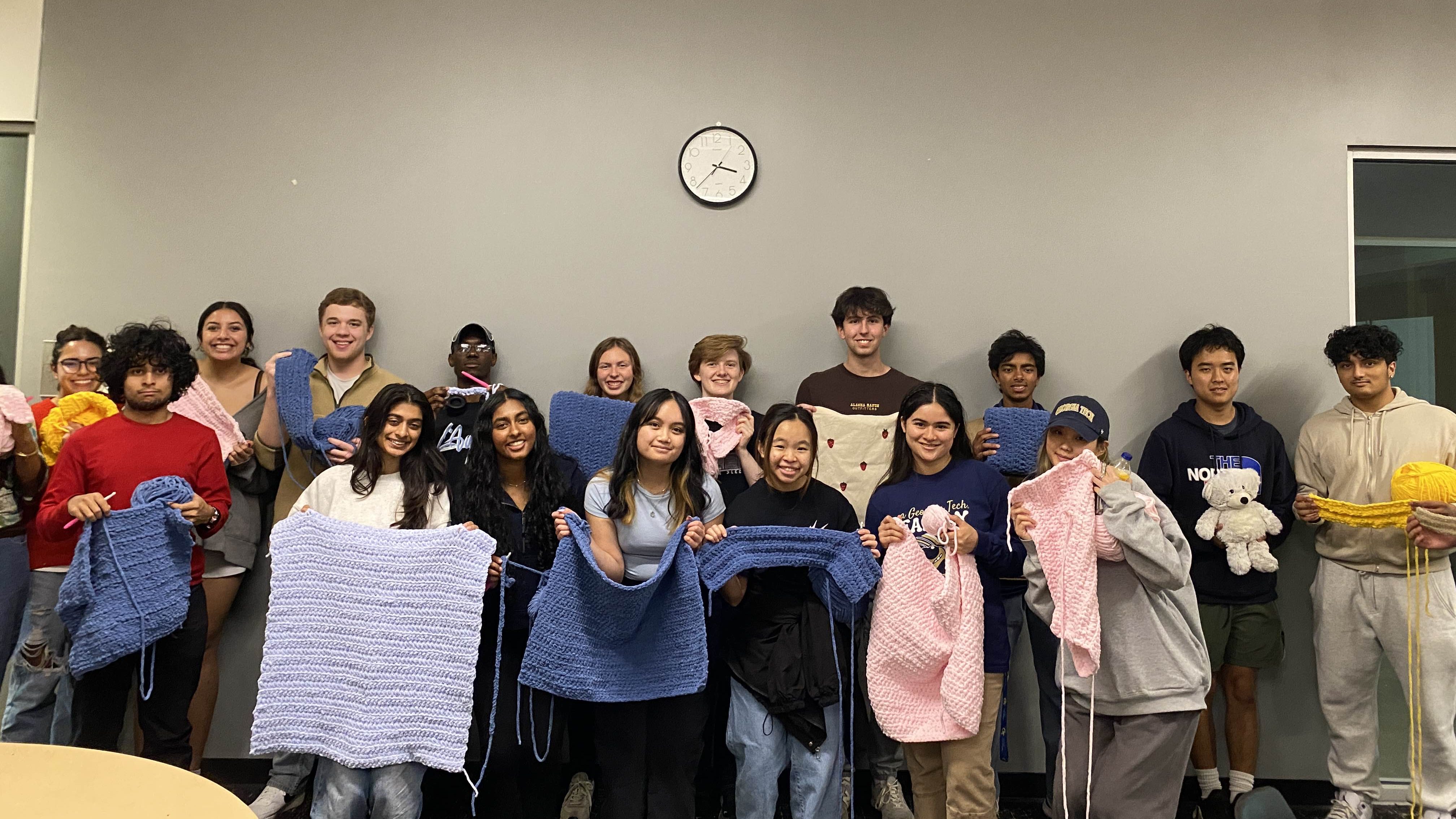 Group of students pose holding completed and in-progress crocheted baby blankets.