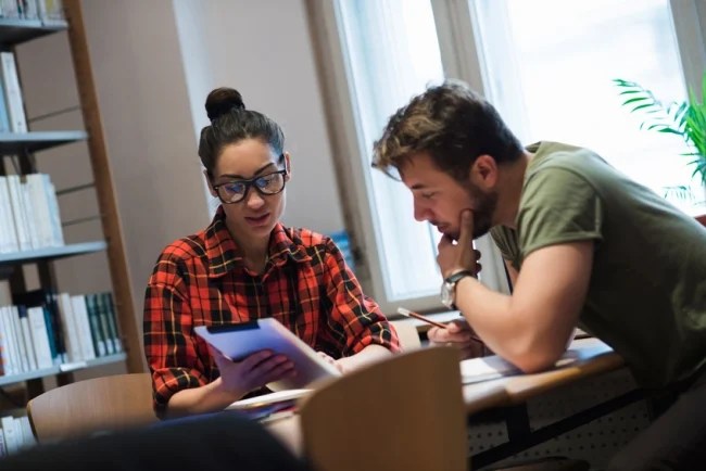 This image showcases a TA and a student who are both having a conversation about an assignment during office hours in an inperson academic setting within the college.