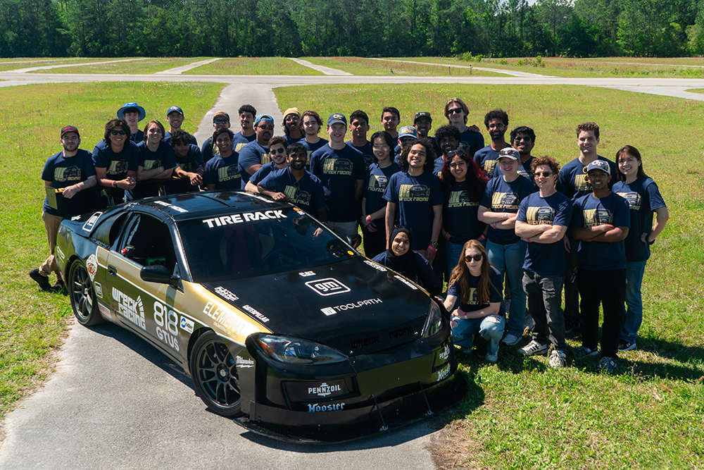Image of a group of GT Wreck Racing club students posed beside a modified race car.