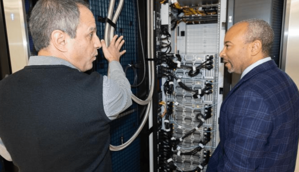 Two men standing in a data center next to an open server rack in the AI makerspace.