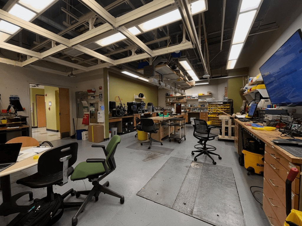 The BME Design shop, with several desks and workbenches with 3d printers on top of them. Several large tool boxes are also placed around the room.
