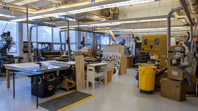 The College of Design Shop, featuring its table saws, band saws, and workbenches. An extensive dust collection system is present throughout the entire space.
