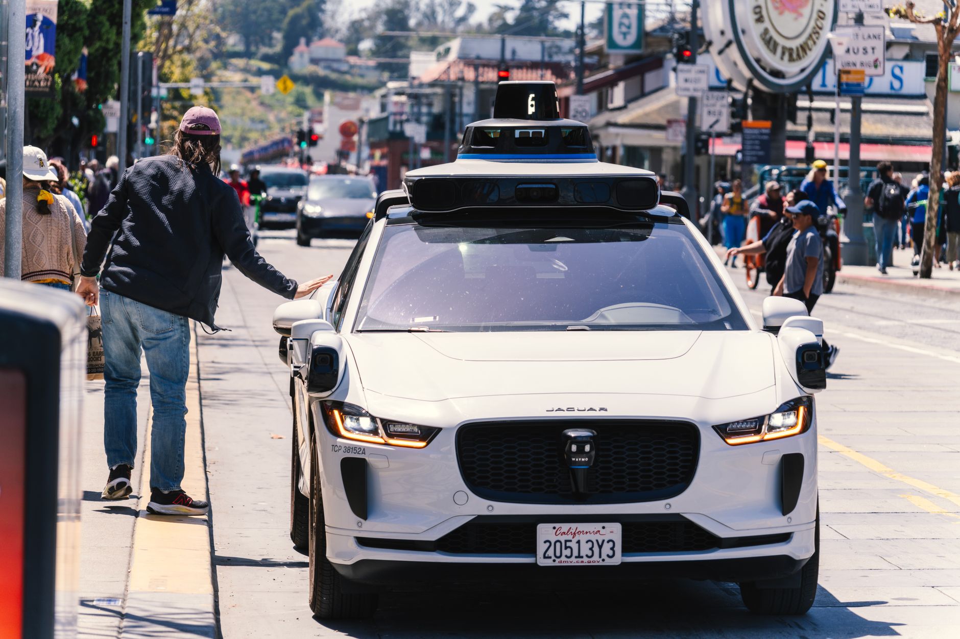 A Waymo vehicle picks up a passenger in a busy city area.
