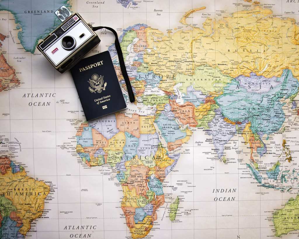 A paper map of the world with camera and passport sitting on top.