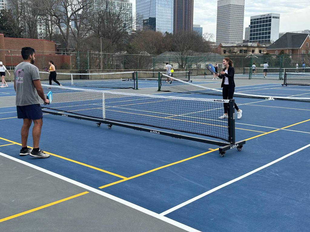 Students playing pickleball outdoor on blue pickleball courts at the top of Georgia Tech’s Peters Parking Deck, and Atlanta buildings visible in the background.