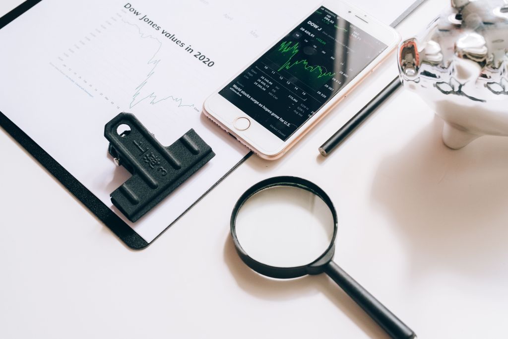 Smartphone displaying stock market data on a document beside a magnifying glass.